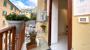 Un balcón con plantas en macetas, una mesita y una puerta que da al interior.