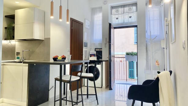 Una cocina moderna con una isla central, iluminación colgante y vistas a un balcón exterior.