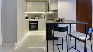 Una cocina moderna con armarios blancos, horno empotrado, estufa a gas y un pequeño comedor con dos sillas.