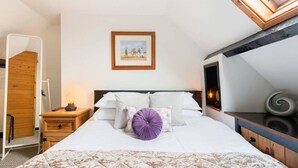 Quarto com cama, mesa de cabeceira com abajur, quadro pendurado na parede e claraboia sobre a cama.