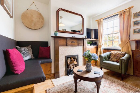 A cozy living room with a fireplace, a sofa, a green armchair, and a round coffee table with a vase of flowers. - Fergies Canal Side Cottage (Warwick)