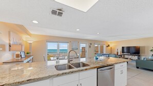 Una cocina moderna con encimeras de granito, electrodomésticos de acero inoxidable y un amplio ventanal con vista al océano.