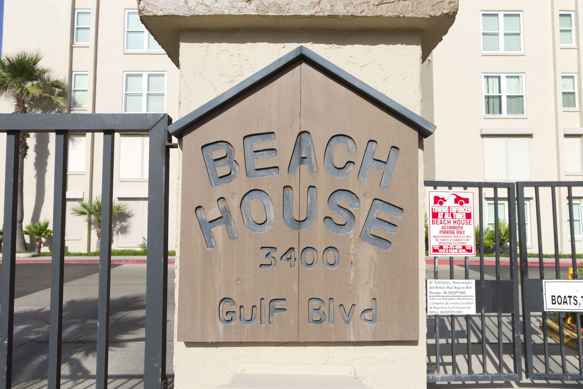 Un senyal de fusta amb la inscripció 'BEACH HOUSE 3400 Gulf Blvd' i una reixa metàl·lica amb un cartell que diu 'TOWING ENFORCED'.