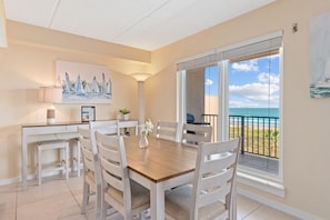 Enjoy meals in this dining area with a table, chairs, and a view of the ocean from the large window and balcony.