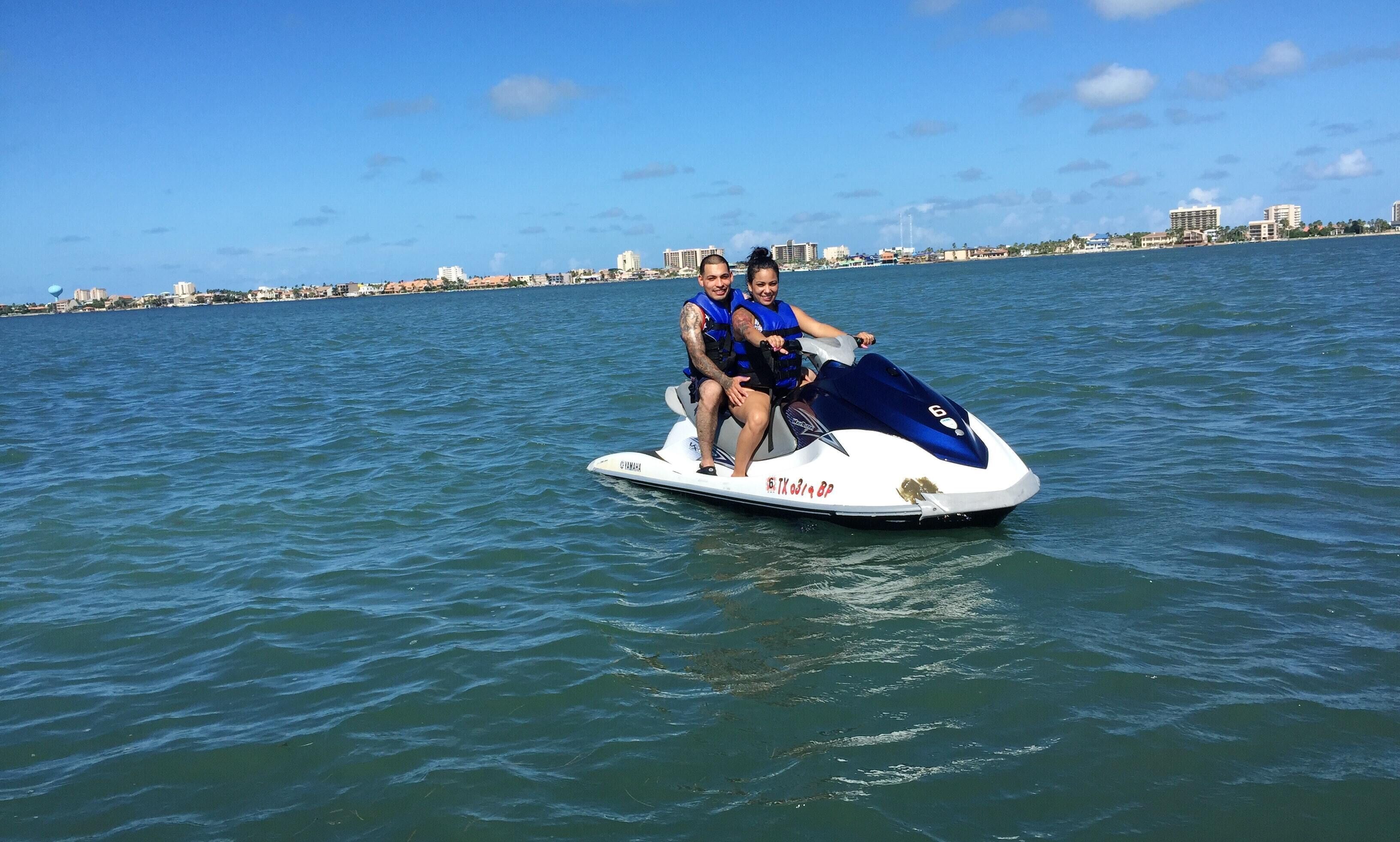 Two people on a jet ski with a cityscape in the background.