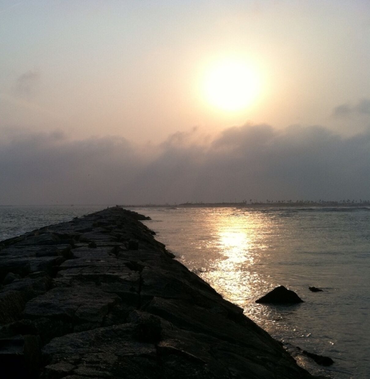 Una costa rocosa con el sol poniéndose sobre el agua.