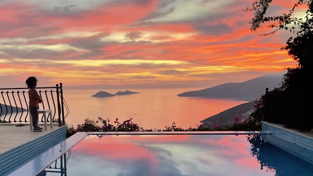 Una piscina infinita con vistas a un atardecer sobre el agua y las colinas.