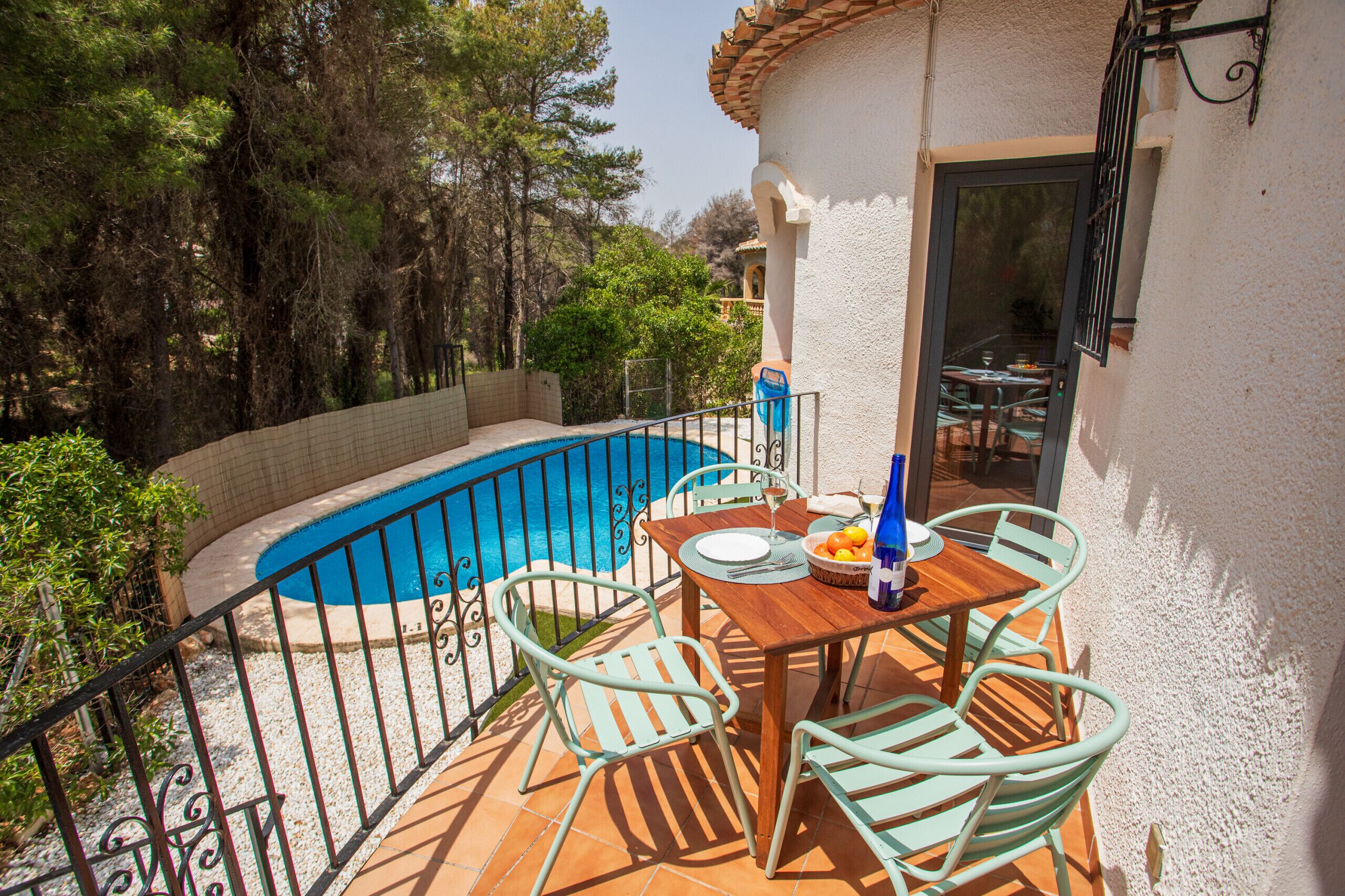 Un área junto a la piscina con una mesa y sillas, rodeada por un muro blanco y una valla de metal.