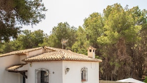 Un pequeño edificio blanco con techo de tejas, piscina y zona de patio.