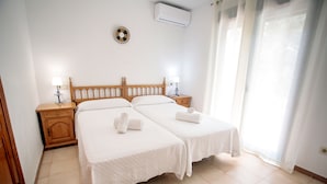 Habitación de hotel con dos camas, cabecero de madera, una mesita de noche con lámpara y una ventana con cortinas.