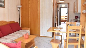 A cozy room with a wooden sofa, a small wooden table, and a dining area with a wooden chair and a small table.