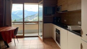 A kitchen with a view of mountains, a dining area with a table and chairs, and a sliding glass door leading to a balcony. - 3-room apartment with balcony in Pra-Loup, private parking (Pra-Loup)