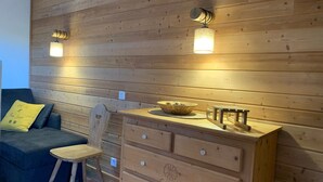 A cozy room with a wooden wall, a blue sofa with a yellow pillow, a wooden chair, and a wooden dresser with drawers. - 3-room apartment with balcony in Pra-Loup, private parking (Pra-Loup)