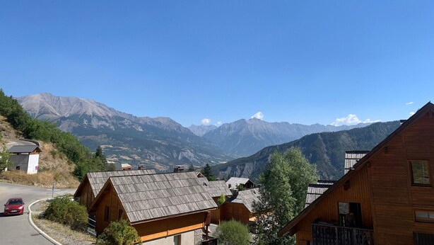 A mountain village with wooden houses, a winding road, and a red car. - 3-room apartment with balcony in Pra-Loup, private parking (Pra-Loup)
