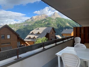 A balcony with a view of mountain houses and a table with chairs.