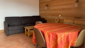 A room with a sofa, a small table, a dining table with a tablecloth, and wooden panel walls. - 3-room apartment with balcony in Pra-Loup, private parking (Pra-Loup)