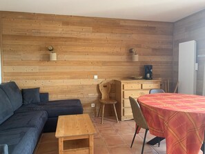 A cozy room with a wooden wall, a sofa, a small table, a desk with a chair, and a dining table with a tablecloth. - 3-room apartment with balcony in Pra-Loup, private parking (Pra-Loup)