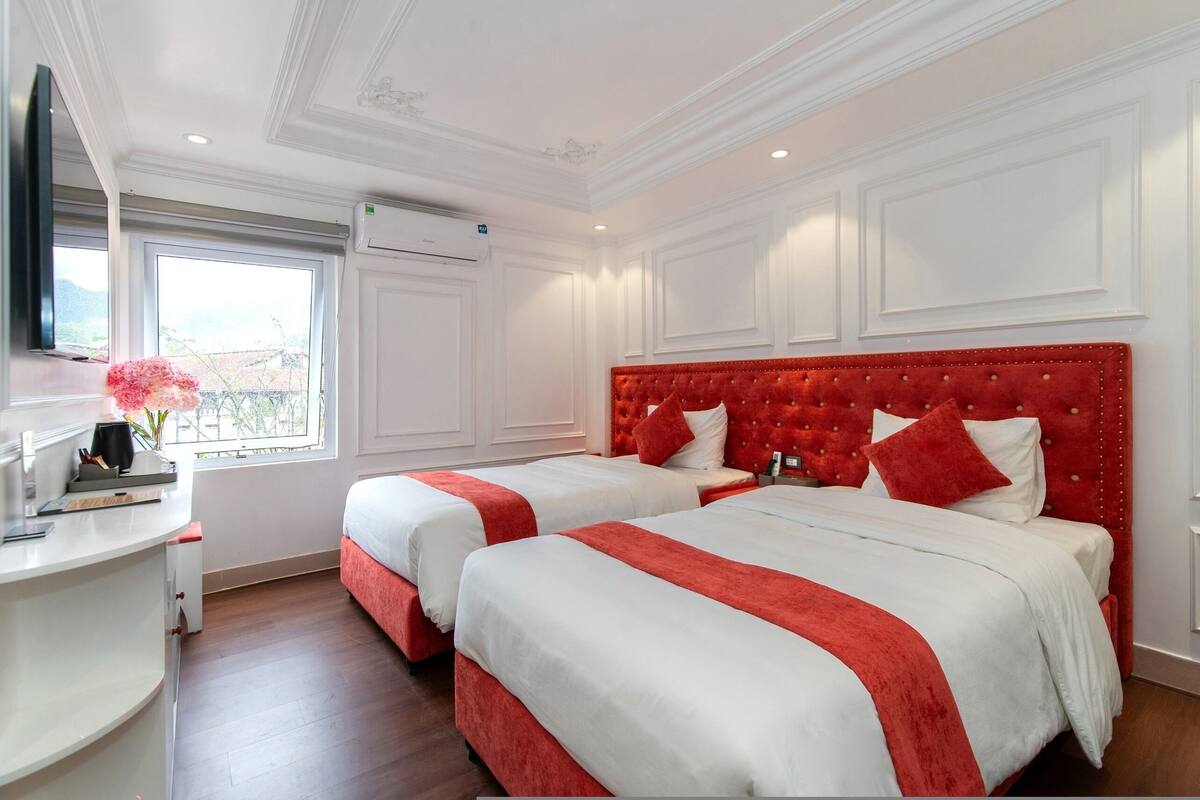 A hotel room with two beds, a desk, and a window with a view.