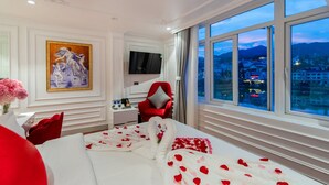 A hotel room with a large bed, a TV, a desk with a chair, and a painting on the wall. - Diamond Hotel Sapa (Sa Pa)