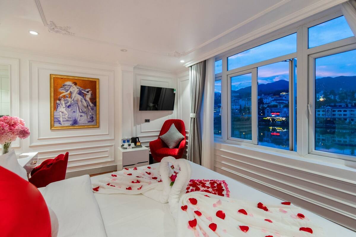 A hotel room with a large bed, a TV, a desk with a chair, and a painting on the wall.