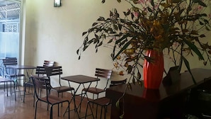 A cafe with tables and chairs, a large potted plant, and a view of the outside. - Diamond Hotel Sapa (Sa Pa)