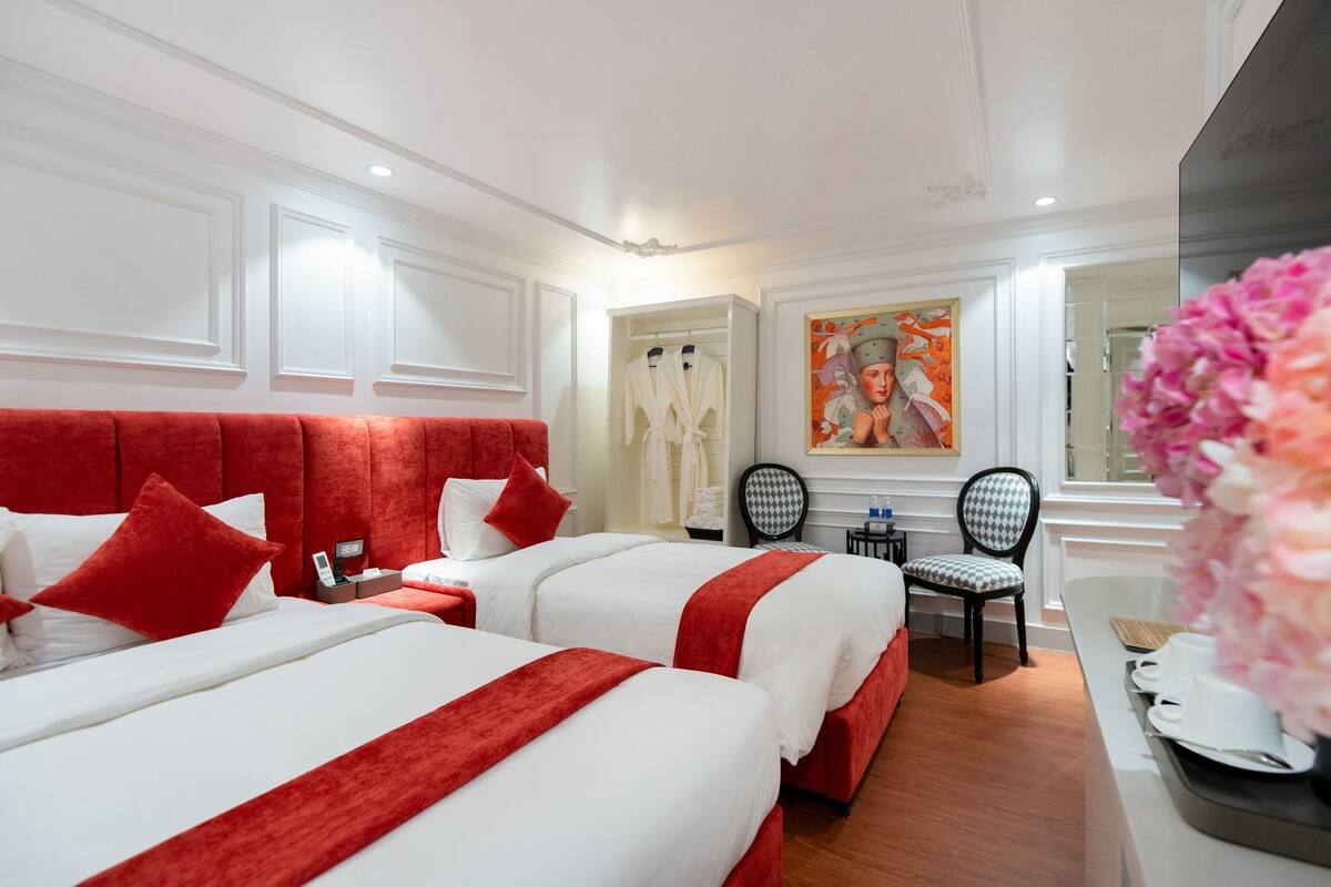 A hotel room with two beds, a red headboard, white walls, a painting, and a mirror.