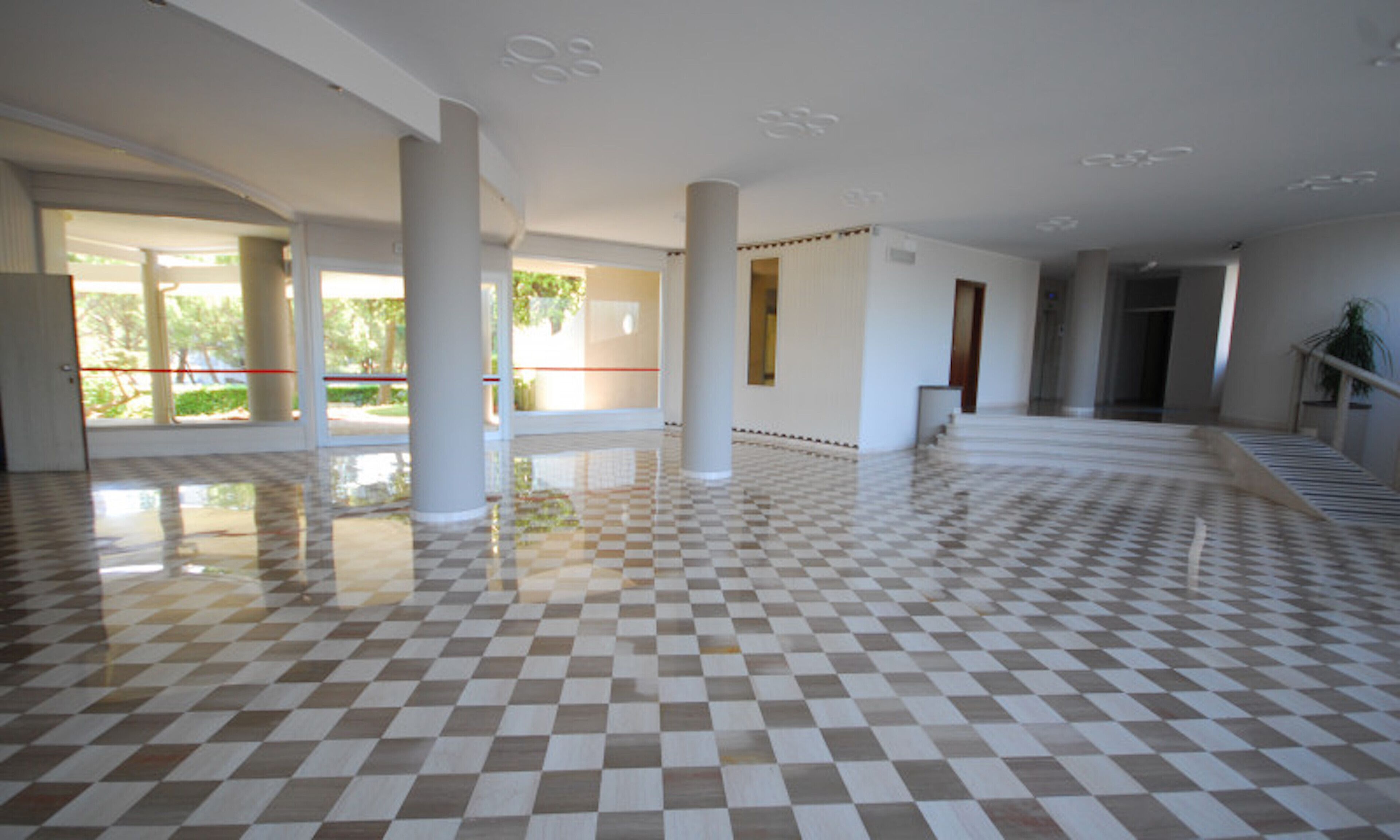 Un'ampia hall con pavimento a scacchi, colonne imponenti e vista sull'esterno.