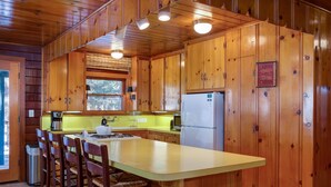 A cabin-style kitchen with wooden walls, a central island with bar stools, a refrigerator, and a window above the sink. - (59) Hansen Cabin at The Redwoods In Yosemite (Yosemite National Park)