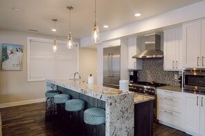 A modern kitchen with a marble island, stainless steel appliances, and bar stools.
