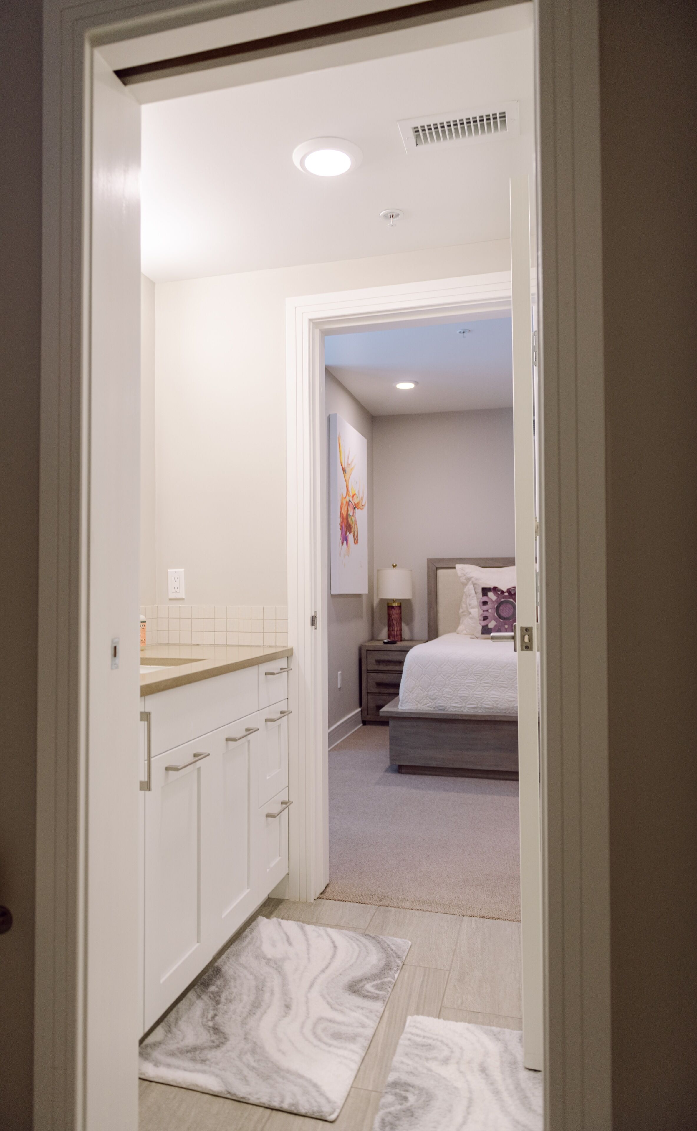 Una habitación de hotel con cama, mesita de noche y baño con lavamanos y armarios.