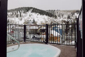 A hot tub on a wooden deck with a view of a snowy mountain and a ski lift in the background.