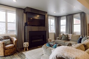 A modern living room with a fireplace, comfortable seating, and large windows.