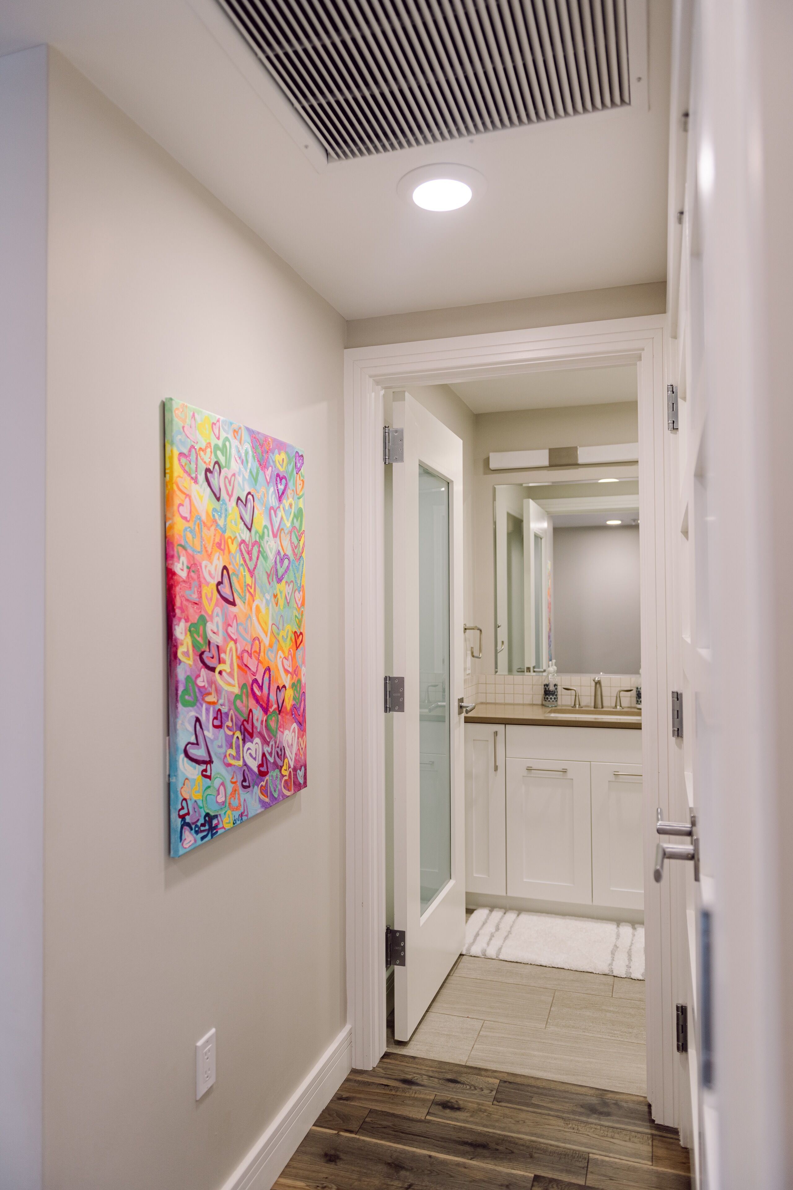 Un pasillo con piso de madera, una puerta blanca y un cuadro abstracto de colores en la pared.