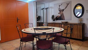 A dining area with a round table, four chairs, a wooden cabinet, a wall-mounted mirror, and a framed deer antler artwork. - Beautiful duplex 65m², 6p, balcony, parking, WiFi (Pra-Loup)