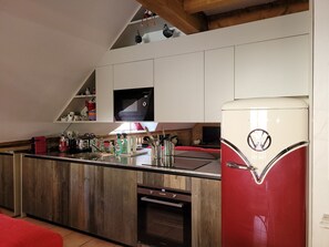 Une cuisine Ă©quipĂ©e dâun four Ă micro-ondes encastrĂ©, dâun rĂ©frigĂ©rateur rouge, de meubles de rangement en bois et dâun plan de travail en bois.