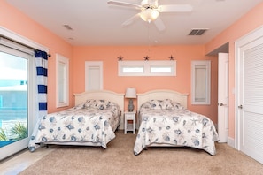 A bedroom with two beds, a ceiling fan, and a view of the outside.
