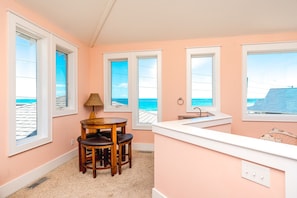 A room with a round wooden table, a lamp, and a view of the ocean through large windows. - 99 Oleander - Luxury 9 BR Home - Great Views, Pool, Hot Tub, Elevator & More! (Surf City)