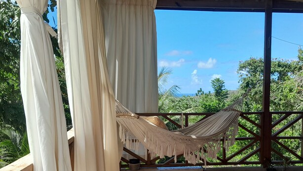 Una hamaca bajo una pérgola de madera con vistas a un follaje exuberante y un cielo azul despejado.