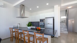 A modern kitchen with a central island, bar stools, a microwave, a refrigerator, and a staircase leading to an upper level. - Coral Beach Villa 5 Bedroom 5 Bathroom 200m from Coast 700m from Coralia Beach (Peyia)