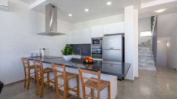 A modern kitchen with a central island, bar stools, a microwave, a refrigerator, and a staircase leading to an upper level.