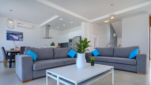 A modern living room with a grey sectional sofa, a white coffee table, and a dining area with a table and chairs. - Coral Beach Villa 5 Bedroom 5 Bathroom 200m from Coast 700m from Coralia Beach (Peyia)