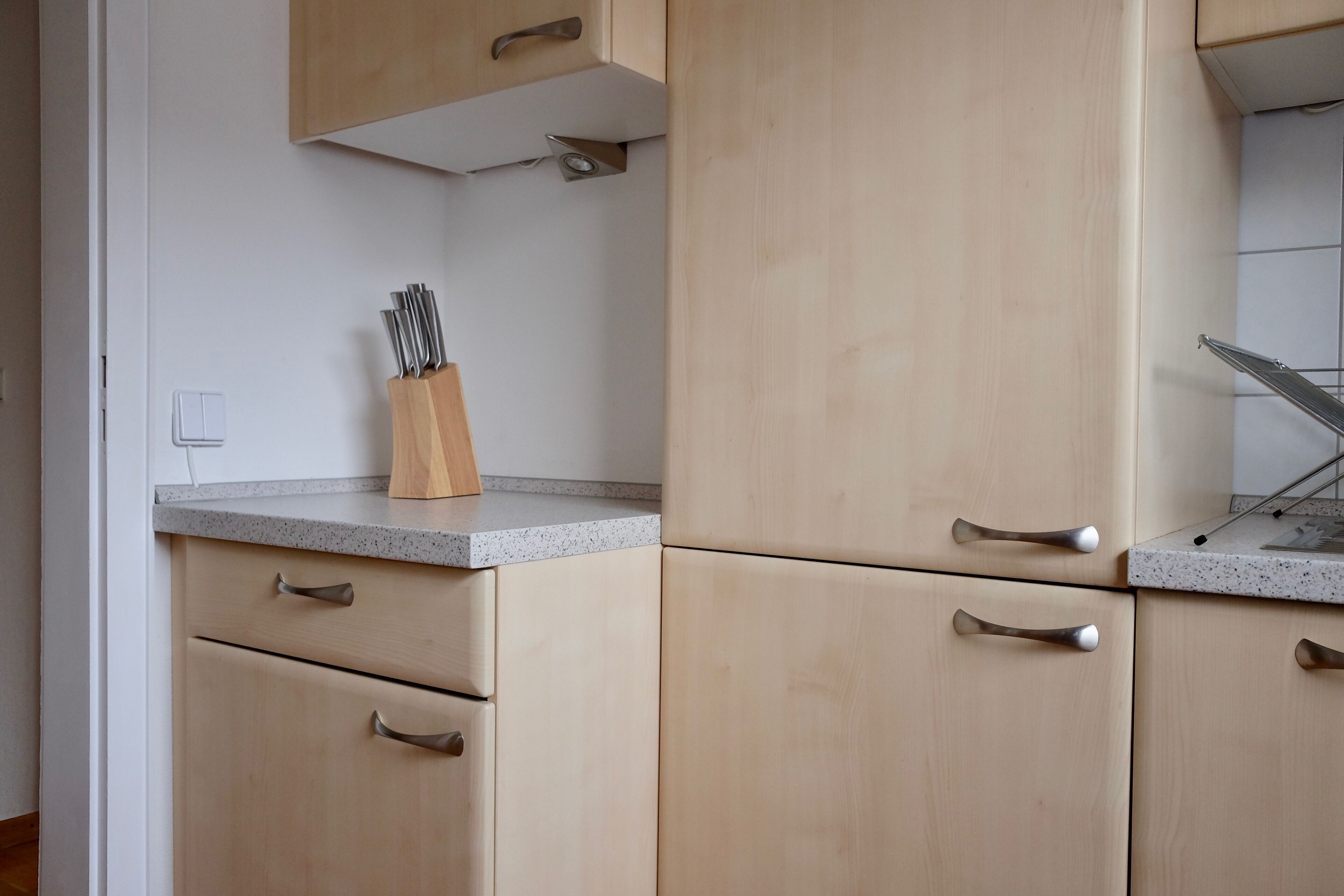 Une cuisine avec des meubles de couleur bois clair, un plan de travail en granit et un bloc à couteaux.