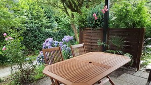 A wooden patio table with four chairs, surrounded by lush greenery and flowering plants. - Stylish apartment in a fantastic location right on Volkspark (FL)