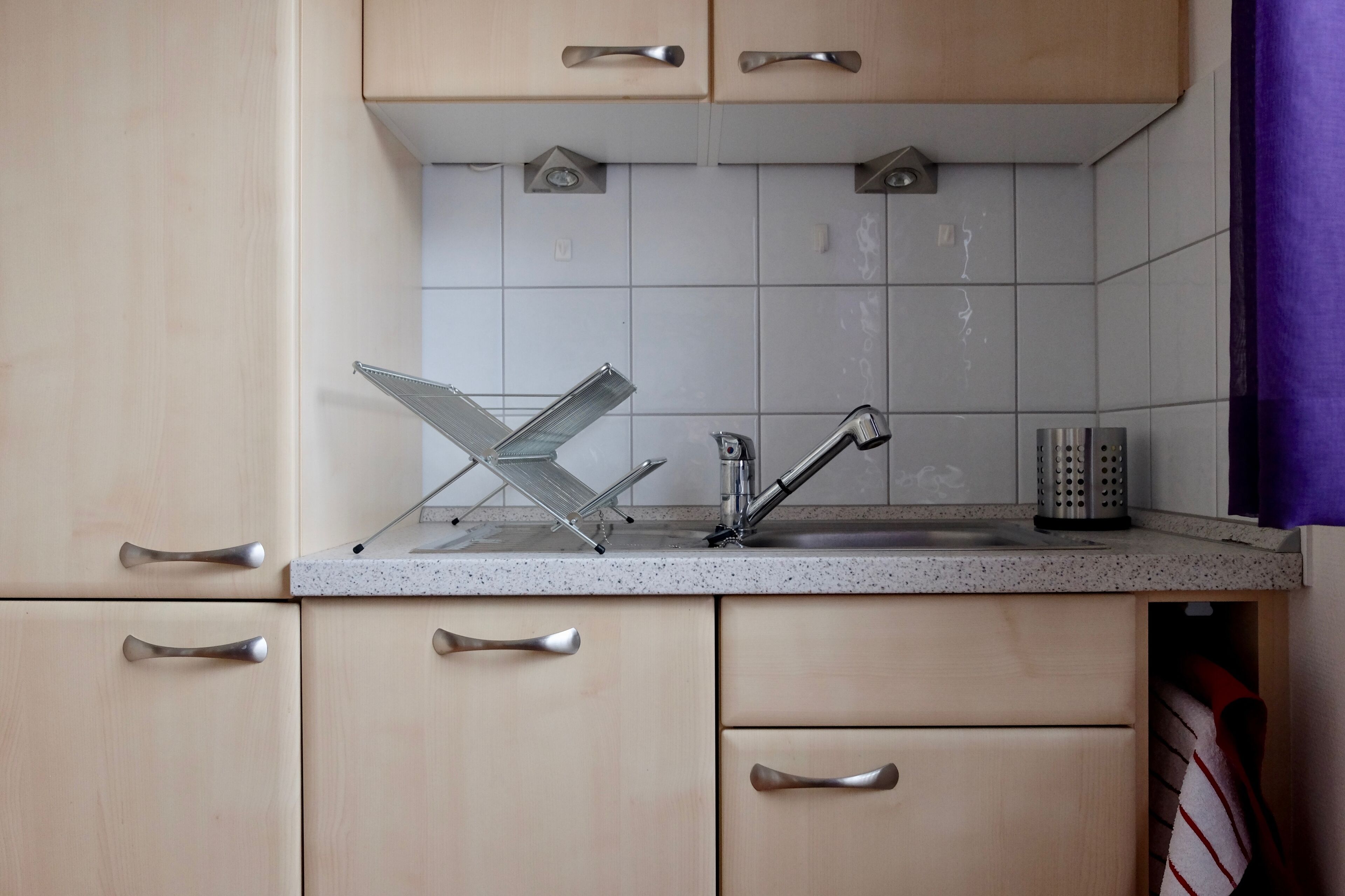 A kitchen with a stainless steel sink, a metal drying rack, and a set of peelers on the counter.