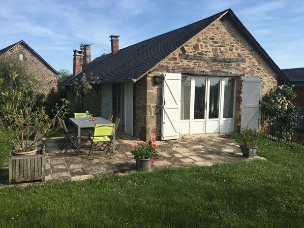Une maison en pierre avec un patio, une table et des chaises, et un jardin.