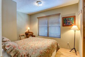 Une chambre à coucher avec un lit, un bureau, une lampe, une fenêtre avec des stores et un tableau au mur.