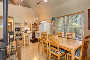 Une cuisine chaleureuse, avec des meubles en bois, un poêle et une grande fenêtre équipée de stores.
