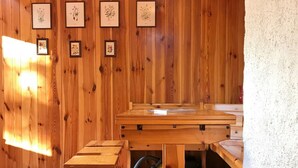 A wooden interior with multiple tables and benches, a red hanging light, and framed botanical prints on the wall.