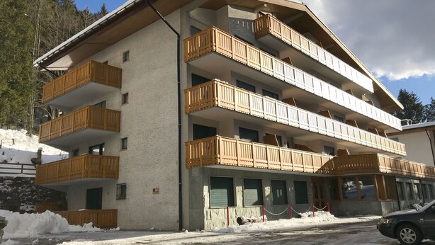 A multi-story building with wooden balconies, a snow-covered ground, and a clear sky.