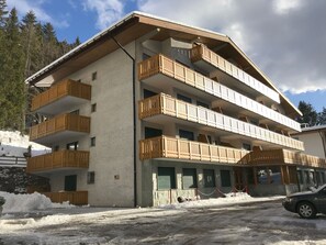 Un edificio de varios pisos con balcones de madera, suelo cubierto de nieve y cielo despejado.